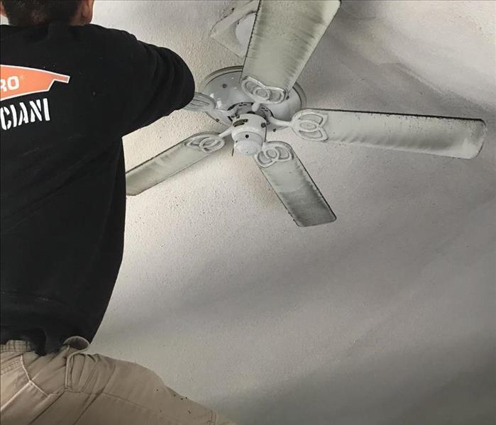 crew member cleaning soot from white fan and ceiling