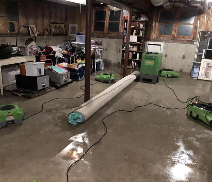 air movers and dehumidifiers drying a flooded unfinished basement with water on concrete floor